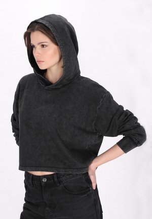 Geknipte zwarte sweatshirt met een capuchon, voorzien van een vervaagde textuur en ribgebreide manchetten. Draagt met hoog-gesneden zwarte denimjeans.