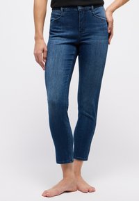 Figurbetonte, knöchellange blaue Jeans aus Denim mit glatter Textur, fünf Taschen und subtiler Ausbleichung am Saum. Klassisches Design mit Knopfverschluss.