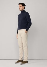 Granatowy sweter z golfem, kremowe chinosy i brązowe zamszowe sneakersy. Strój charakteryzuje się dopasowanym krojem i teksturowanym materiałem bez widocznych wzorów.