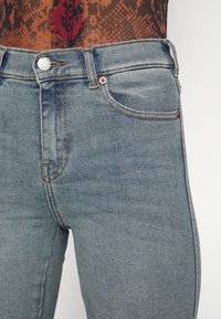 Blauwe high-waisted jeans met een gladde textuur, voorzien van een zilveren knop, contrasterende stiksels en zijzakken.