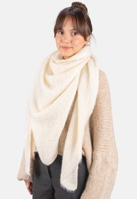 Écharpe blanc cassé en tissu doux et texturé, drapée dans une forme triangulaire surdimensionnée. Présente des détails de tissage subtils et des bords frangés.