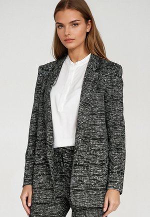 Czarno-biała teksturowana marynarka o dopasowanym fasonie, z wyciętymi klapami i zapięciem na jeden guzik, w połączeniu z białą bluzką.