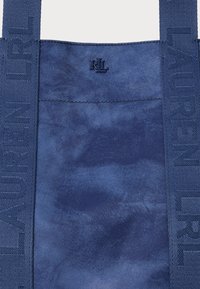 Näbblå tygväska med en texturerad yta, med kraftig "LAUREN LRL" märkning på banden och en liten präglad logotyp på framsidan.