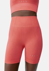 Korallfärgade atletiska shorts gjorda av stretchigt tyg med hög midja. Har flatlocksömmar och en liten reflexlogotyp nära botten.