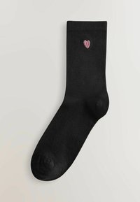 Calcetín de algodón negro con un pequeño diseño de corazón bordado en rosa cerca del puño. Textura suave, forma de calcetín estándar.