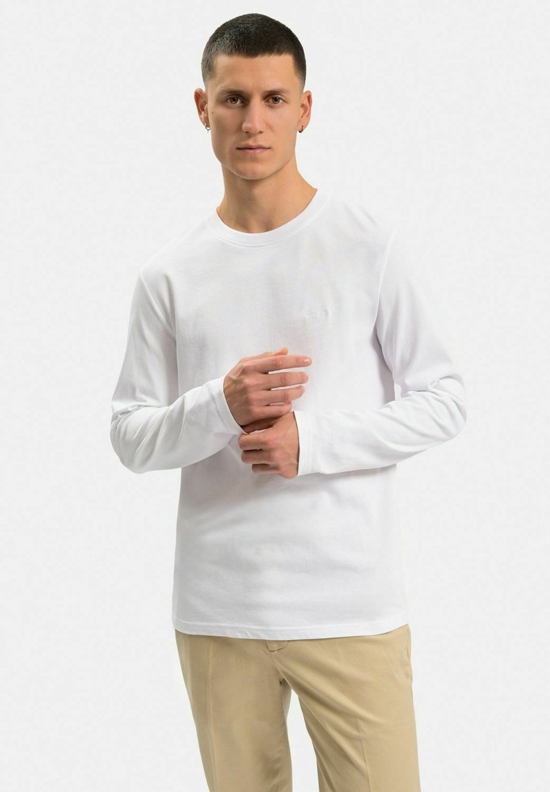 Langærmet hvid bomulds t-shirt med rund hals, tætsiddende pasform og minimalistisk design. Båret med beige bukser.