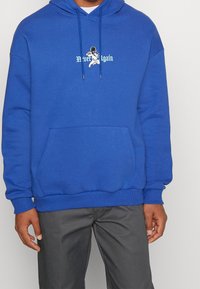 Felpa con cappuccio blu in cotone, con cappuccio con coulisse, tasca frontale e stampa grafica con la scritta "Mai Più" sul petto.