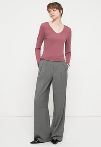 Μακρυμάνικο τοπ σε μωβ απόχρωση με V λαιμόκοψη και τριγωνική ρίγα στο τελείωμα, συνδυασμένο με ψηλόμεσες, φαρδιές γκρι παντελόνες με πιέτες και πλευρικές τσέπες.