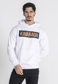Biely mikina s kapucňou, na prednej strane s veľk�ým čiernym obdĺžnikom, na ktorom je napísané slovo "KAVANAGH" textúrovaným zlatým písmom. Na prednej strane je klokaní vrecko.