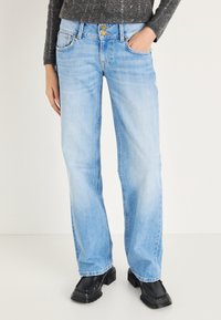 Vaqueros de mezclilla azul claro con corte recto, acabado desgastado, cierre de doble botón, bolsillos delanteros y detalles de costura.