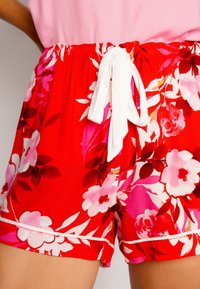 Röda blommiga shorts med ett vitt dragsnöre, prydda med rosa och vita blommor. Lätt material med en avslappnad passform och fåll.