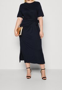 Laivastonsininen midimekko, jossa on lyhyet hihat, kiertynyt etuosan yksityiskohta ja sivuhalkaisija. Yhdistetty metallinhohtoiseen kultaan väriseen clutch-laukkuun ja mustiin nilkkaremmeillä varustettuihin korkokenkiin.