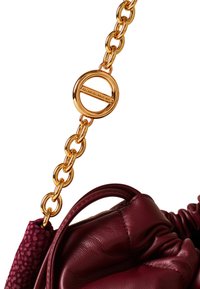 Burgunderfarbene Lederhandtasche mit einer goldenen Kettenriemen, ausgestattet mit einem markanten runden Hardware-Tag und strukturierten Akzenten auf einer Seite.