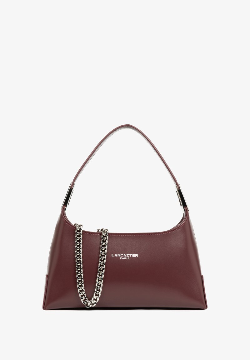 Sac à main en cuir bordeaux avec une texture lisse, une poignée courbée et un accent en chaîne argentée. Présente un logo embossé sur le devant.