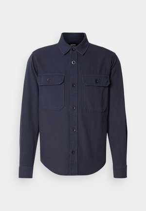 Tamsiai mėlynas ilgomis rankovėmis marškiniai, pagaminti iš švelnios medžiagos, su smailiu apykakle, sagčių užsegimu priekyje ir dviem krūtinės kišenėmis su užsegimais.