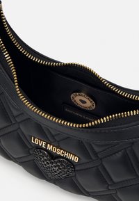 Black quilted leather bag with gold hardware, featuring a heart accent and logo plaque inside the zippered compartment.