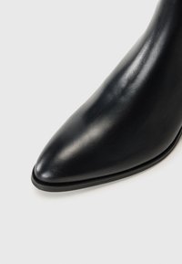 Stivaletto in pelle nera alla caviglia con punta appuntita, texture liscia e tacco sottile, caratterizzato da una cucitura sottile lungo il bordo.