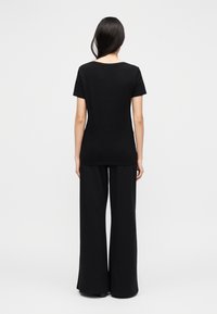 Μαύρο κοντομάνικο μπλουζάκι από απαλό ύφασμα, με στρογγυλή λαιμόκοψη, σε συνδυασμό με μαύρο φαρδύ παντελόνι που ρέει, σε προβολή από πίσω.