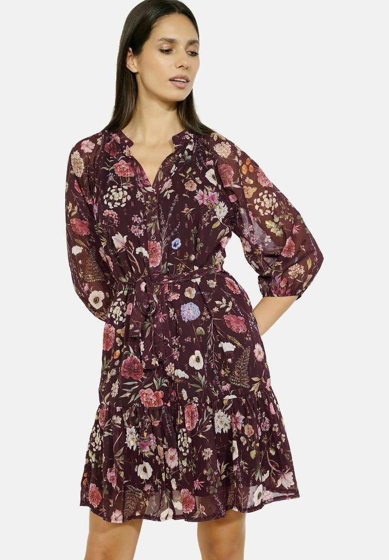 Abito fluido al ginocchio in chiffon bordeaux scuro, con motivi floreali multicolori, colletto, chiusura con bottoni e vita con cintura.