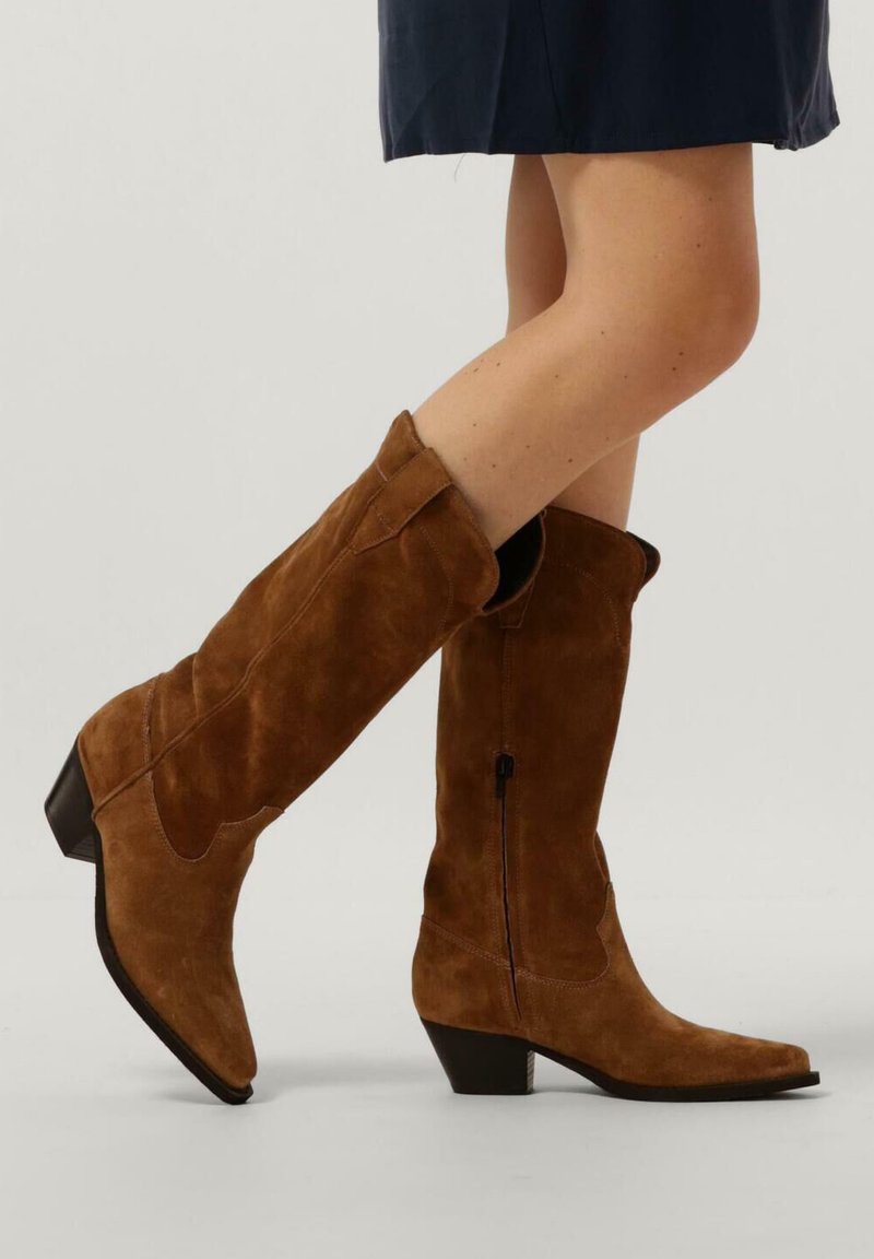 Braune Wildleder-Stiefel bis zum Knie mit spitzen Zehen, einem leichten Absatz und einem seitlichen Reißverschluss. Sie verfügen über Nähdetails und einen flexiblen Schaft.