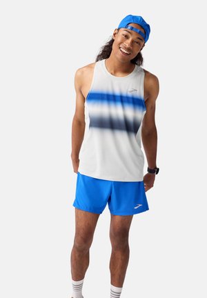 Männliches Sportoutfit bestehend aus einem ärmellosen weißen Tanktop mit einem blauen Ombre-Design und einheitlich blauen Shorts, ergänzt durch eine blaue Kappe.