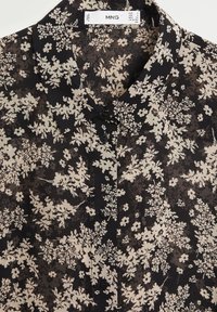 Blouse noire à fleurs en tissu léger avec col, présentant des motifs floraux beiges, une fermeture à boutons et une coupe décontractée.