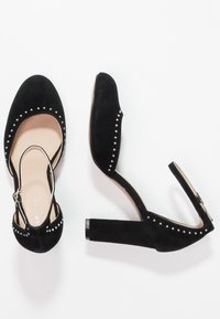Svarta mocka högklackade skor med rund tå, med nitar längs sidorna och justerbart ankelsnöre.