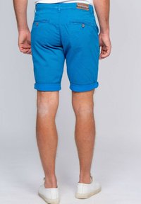 Shorts en coton bleu avec des ourlets retournés, deux poches arrière avec fermetures à bouton et une étiquette en cuir de marque sur la taille.