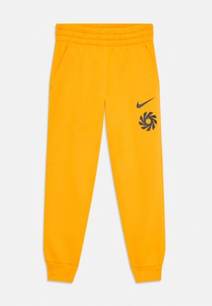 Dzelteni flīsa sporta bikses ar elastīgu jostasvietu un aprocēm, sānu kabatām, un melno Nike svītru un grafisko logotipu kreisajā augšstilbā.