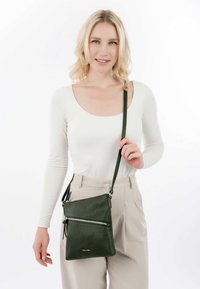 Grüne Leder-Crossbody-Tasche mit strukturierter Oberfläche, ausgestattet mit zwei Rei�ßverschlusstaschen und einem verstellbaren Trageriemen.