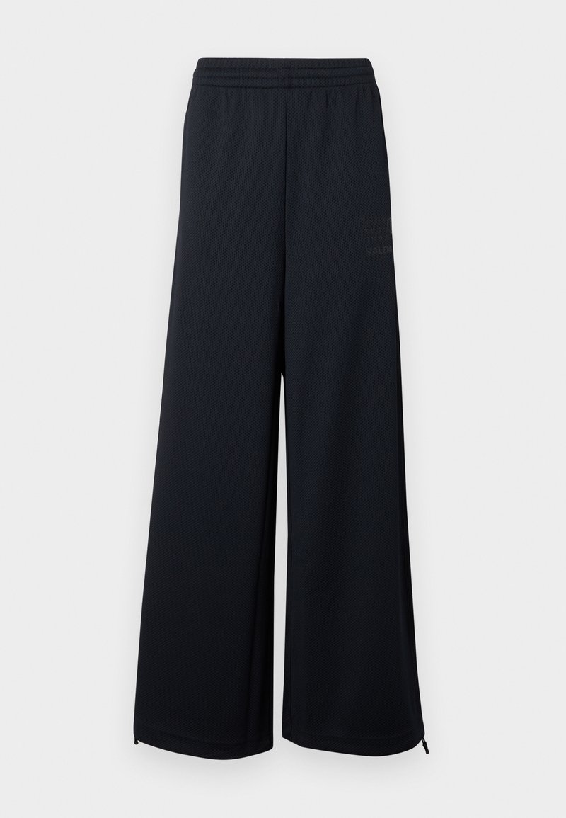Pantalons larges en mesh noirs avec une taille élastique et de petites fermetures éclair aux ourlets, présentés sur un fond blanc.