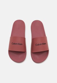 Sandale roșii cu talpă din cauciuc, cu un brâu lat și logo-ul „Calvin Klein” embosat. Talpă interioară moale și texturată pentru confort.