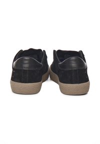 Sneaker nere in suede con suola in gomma marrone testurizzata, tacco rotondo e design minimalista senza branding visibile.