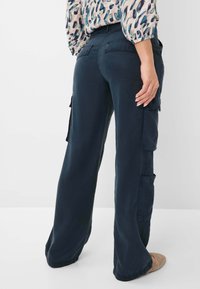 Marine cargobroek met wijde pijpen, voorzien van zijzakken en een gladde textuur. Gecombineerd met een blouse met een multi-kleurig patroon.