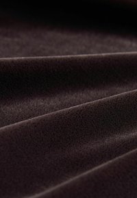 Brauner Stoff mit einer weichen, samtigen Textur, der subtilen Falten und einer glatten Oberfläche aufweist. Die Farbe ist tief und einheitlich und reflektiert das Licht sanft.