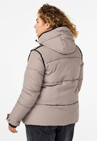 Giubbotto imbottito color beige chiaro con cappuccio, caratterizzato da accenti neri lungo le spalle e i polsini, e imbottitura trapuntata per l'isolamento.