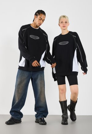 Dve modelky majú na sebe zladené oversized čierne a biele mikiny; jedna ich kombinuje s voľnými džínsami a teniskami, druhá s čiernymi šortkami a čižmami.