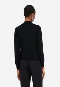 Pullover nero in maglia con maniche lunghe, leggermente costolato ai polsini e all'orlo, caratterizzato da un colletto classico e una texture liscia e morbida.