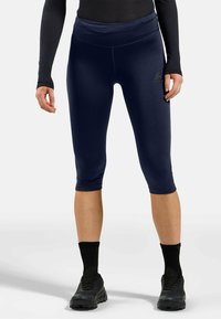 Marinefarbenes, knöchellanges Leggings aus dehnbarem Material mit glatter Textur; hoher Bund; Logo auf dem linken Oberschenkel gedruckt; kombiniert mit schwarzen Schuhen.