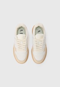 Hvite sneakers med beige detaljer, mykt materiale, perforeringer på tåen, og flate lisser. Gummisåle med en lys brun nyanse.