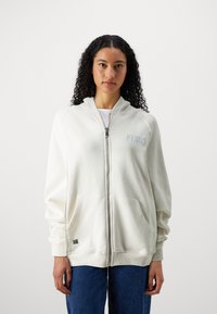 Felpa bianca con zip realizzata in tessuto morbido. Presenta ampie tasche frontali, polsini a costine e un logo sottile di colore azzurro chiaro sul petto.