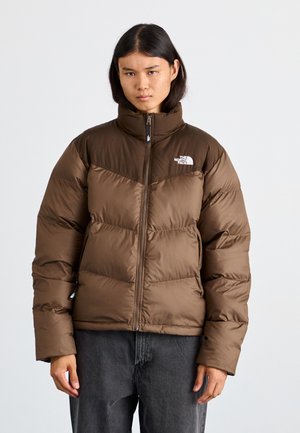 Veste matelassée marron avec un col haut, fermeture éclair sur le devant et motif en chevrons. Comprend un logo sur la poitrine gauche et des poignets côtelés.