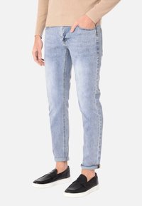 Jeans in denim blu chiaro con una vestibilità slim, leggermente sbiaditi, e risvolti, abbinati a scarpe slip-on nere con una finitura testurizzata.