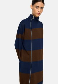 Sweterek w paski z dzianiny z wysokim kołnierzem. Posiada poziome paski w kolorze granatowym i brązowym, zamek błyskawiczny na całej długości oraz luźny krój.