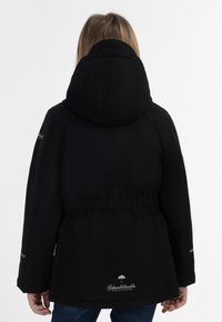Svart vattentät jacka med huva, elastisk midja och logodetalj vid fållen. Tyget verkar slätt och matt.