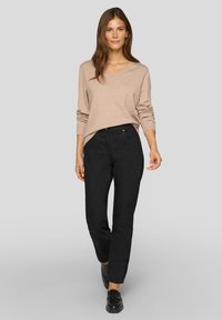 Beiger V-Ausschnitt-Pullover, kombiniert mit schwarzen, gerade geschnittenen Hosen. Glatte Texturen mit einfachem Design. Schwarze Loafers vervollständigen das Outfit.
