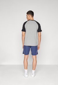 Gray and black raglan t-shirt with short sleeves paired with blue shorts featuring side accents and white sneakers. Minimalist design.