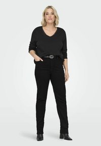 Musta pitkähihainen paita V-pääkohdalla ja pitsireunalla, yhdistettynä korkeavyötäröisiin mustiin farkkuihin ja mustiin korkokenkiin nilkkapituudella, jossa on kaksirenksinen vyö.