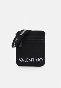 Svart rektangulær crossbody-veske med frontlomme med glidelås, hvit VALENTINO-logo og svart stropp med gjentatt VALENTINO-tekst.