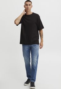 Sort kortærmet ribbet t-shirt med rund hals, parret med lyseblå lige ben jeans og sorte sneakers. Bemærkelsesværdige tatoveringer på armen.